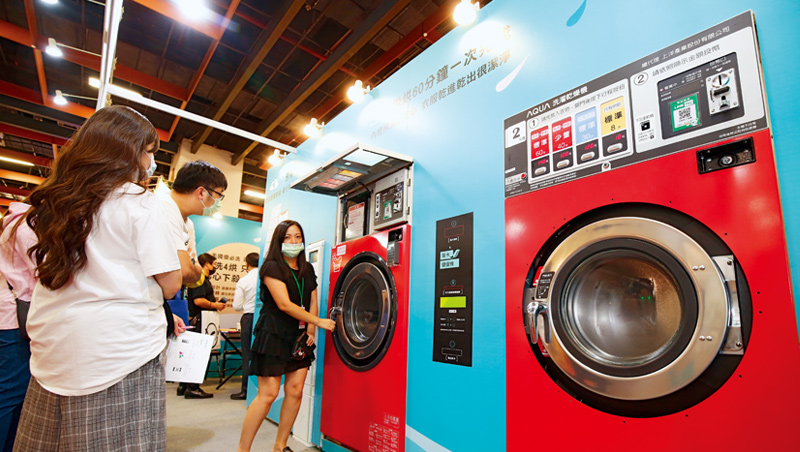 10月台北國際加盟展中，自助洗衣店加盟總部員工，正向加盟主說明洗脫烘三合一的洗衣設備優勢。